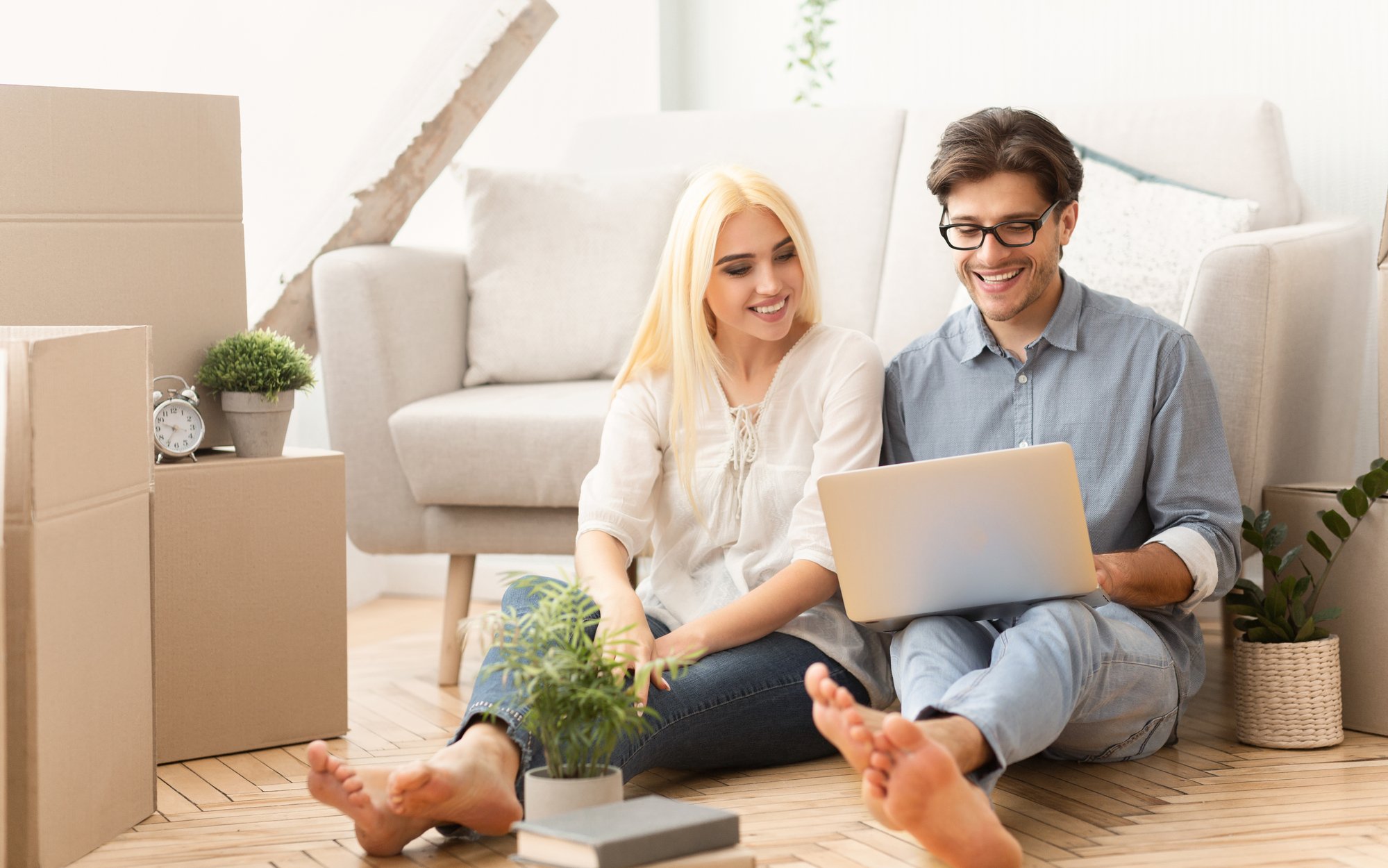 Cheerful couple sitting on floor using laptop in new house